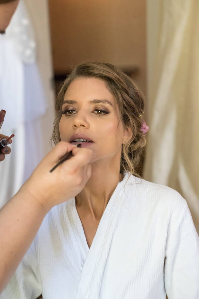 Expert hair and makeup artist applies lipstick to a bride